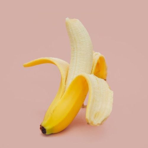 A single peeled banana standing upright against a light pink background