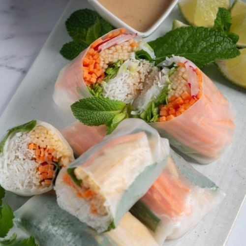 Fresh vegetable summer rolls cut in half, revealing fillings of vermicelli noodles, carrots, beansprouts, and herbs.