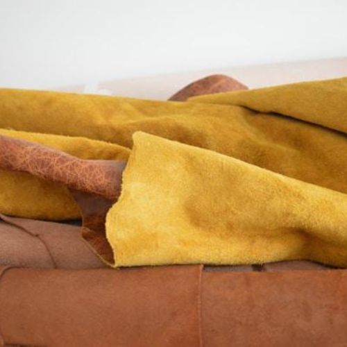 Several large pieces of leather hide in shades of mustard yellow and brown, draped over one another in a casual arrangement