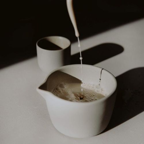 A minimalist scene with milk being poured into a white ceramic pitcher