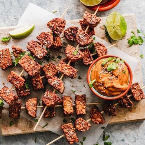 A selection of skewered tempeh cubes sprinkled with sesame seeds, beautifully arranged on a wooden board