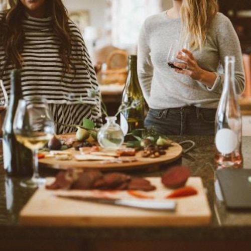 A group of women gathered around a kitchen island with wine glasses and plates of appetizers